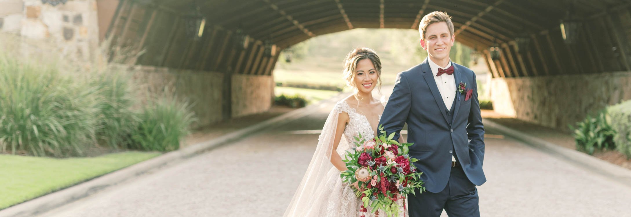 Bella Collina Happy Smiling Couple with Bouquet in Front of Bridge